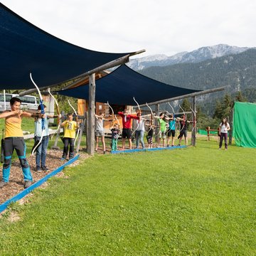 Numerous kids practicing their aiming skills at the canopied practice area of the 3D archery course. 