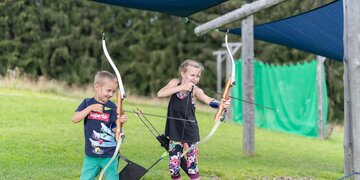 Two kids practicing their skills with bow and arrow at the practice area on Wurbauerkogel.  | © Hinterramskogler