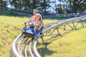 A mother and daughter swooshing downhill on a two-person sled on the Alpine Coaster.  | © Hinterramskogler