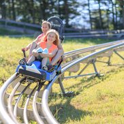 A mother and daughter swooshing downhill on a two-person sled on the Alpine Coaster.  | © Hinterramskogler