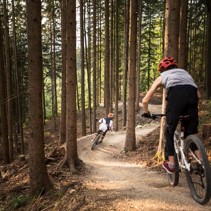 Zwei Biker, die hintereinander den Singletrail am Wurbauerkogel durch den Wald flitzen. | © Roland Haschka